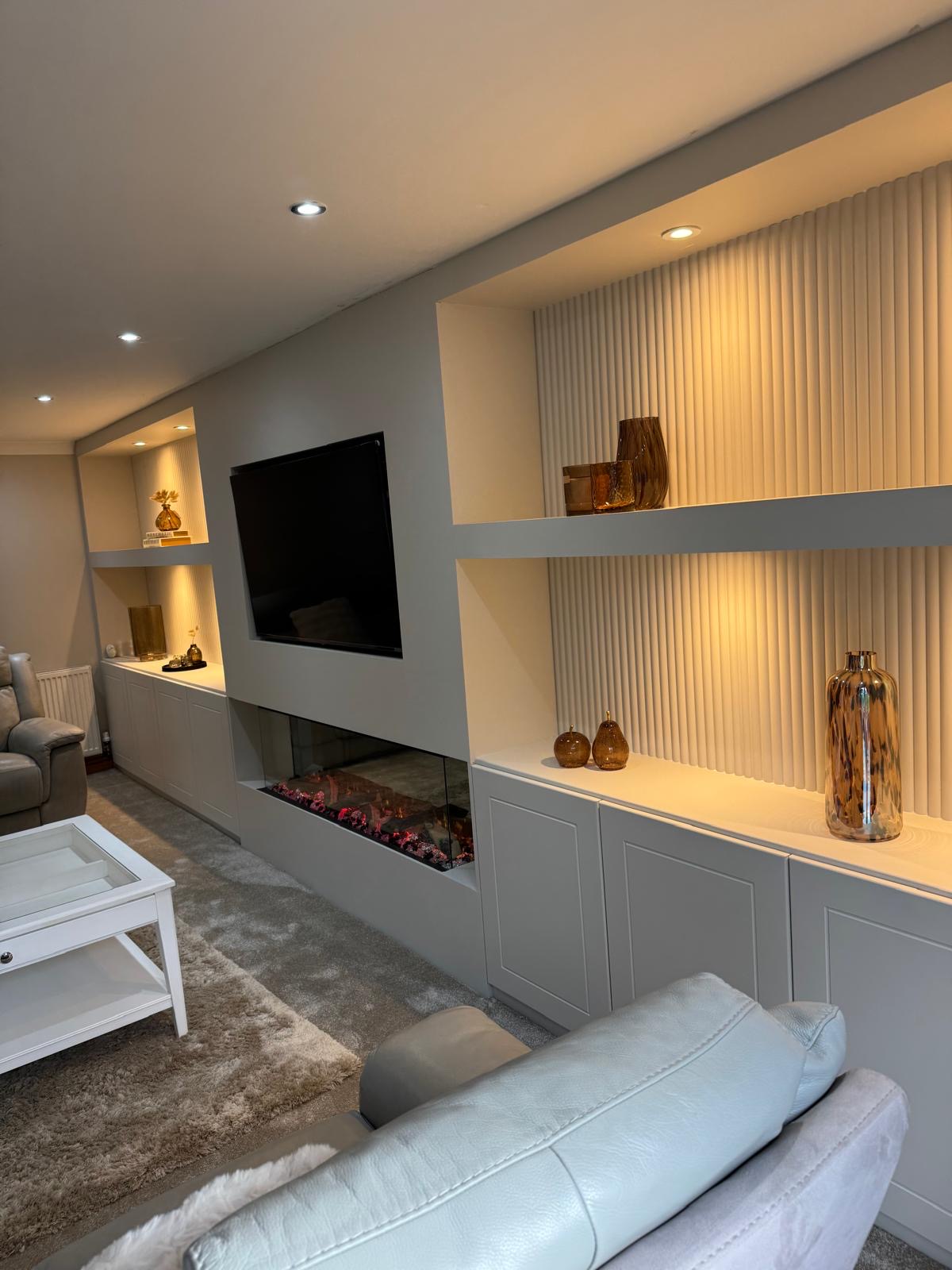 Bespoke reeded grey media wall with warm backlit shelving and linear fire by SM Bespoke Interiors, Birmingham