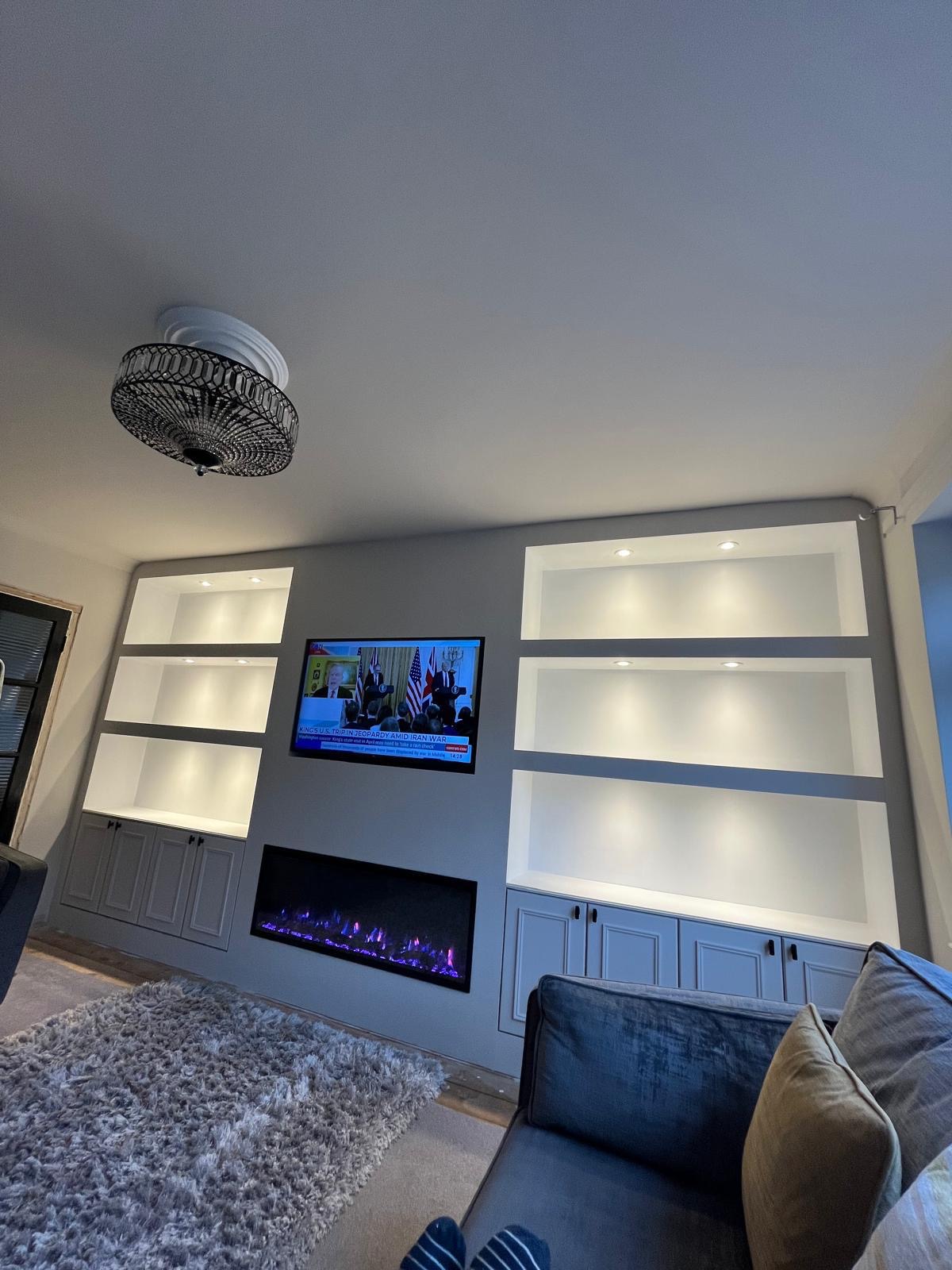 Bespoke white media wall with symmetrical backlit shelving and linear electric fire