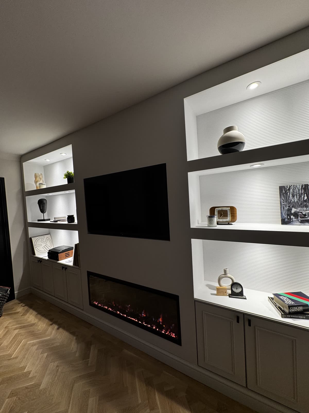 Bespoke media wall with lit fluted-back shelving, a recessed TV and a linear electric fire above a herringbone floor