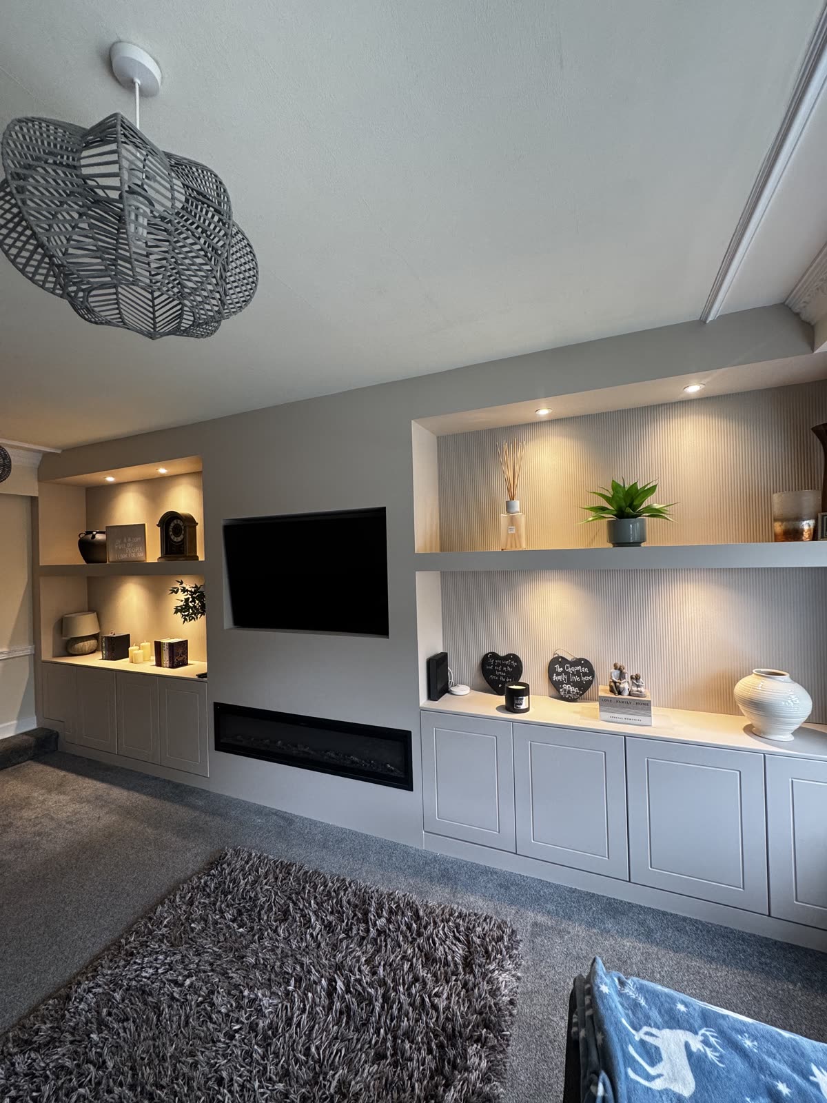 Grey media wall with lit fluted-back shelving, cupboards below, a recessed TV and a linear electric fire