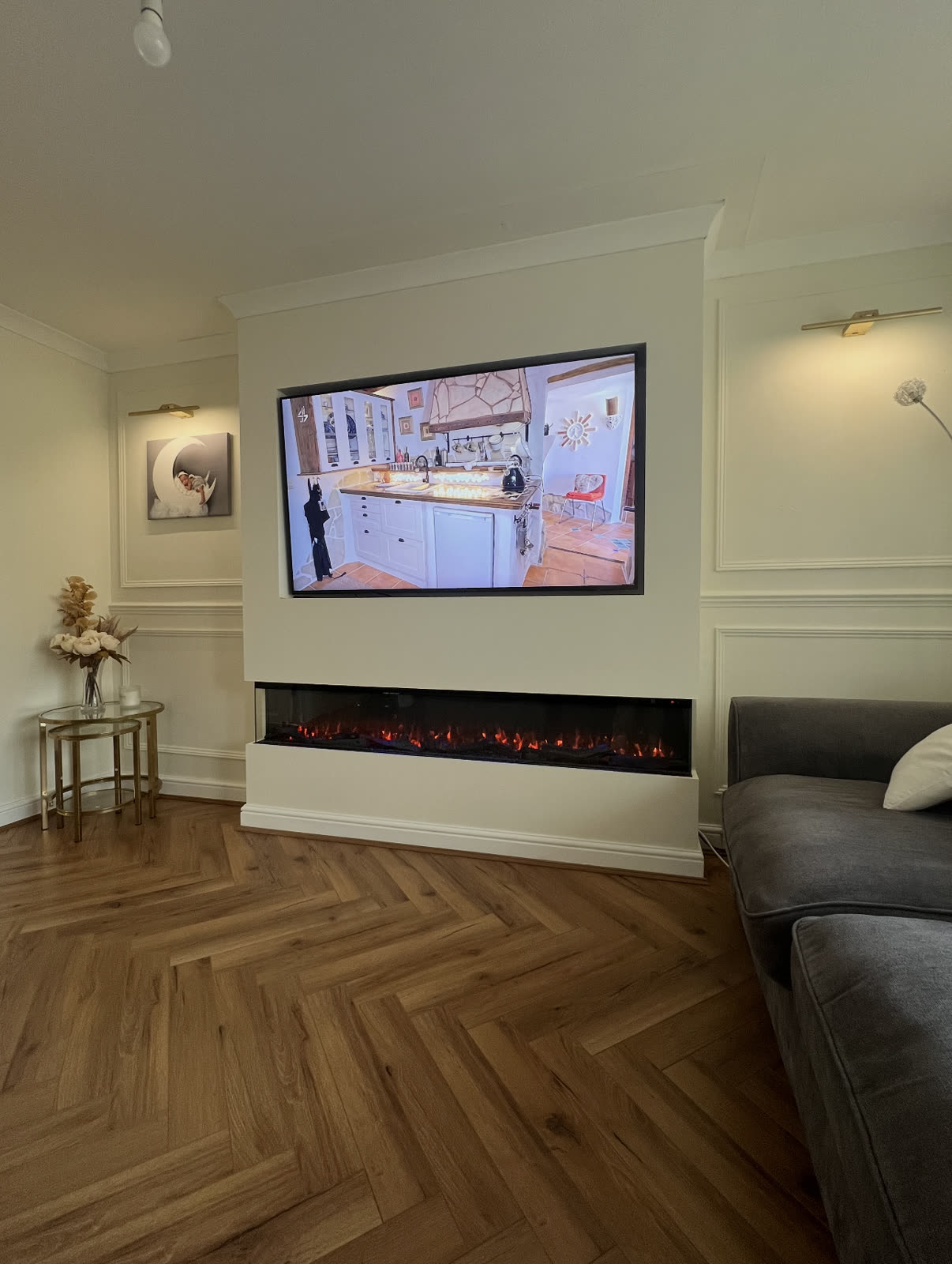 Chimney-breast media wall with a wall-mounted TV over a wide electric fire, panelled walls and herringbone floor