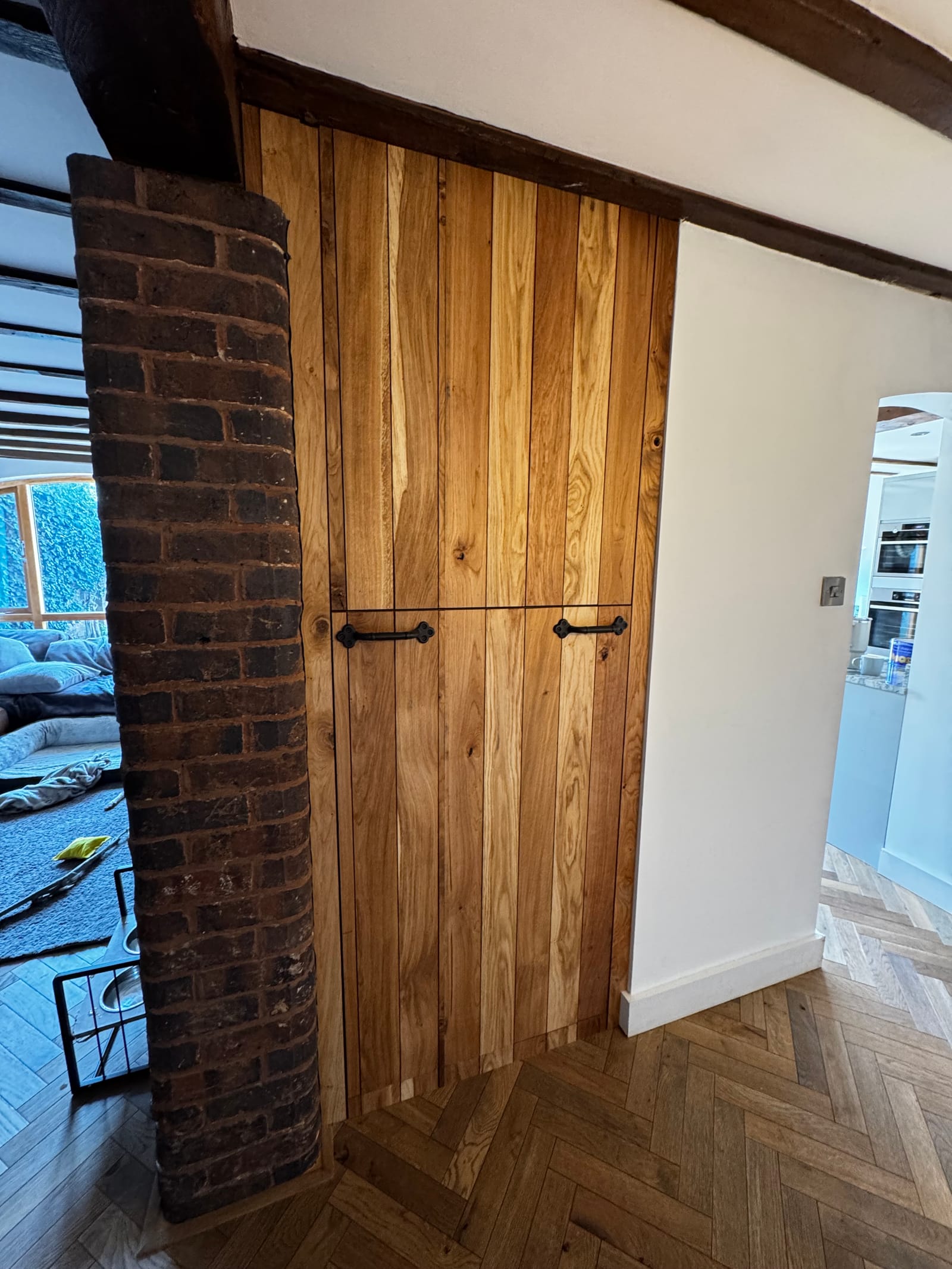 Bespoke oak slat under-stair door beside an exposed brick chimney in a period cottage