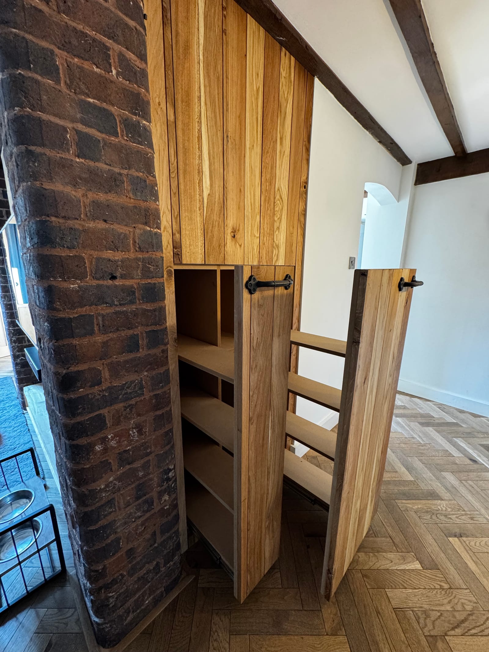 Oak slat under-stair storage with doors open revealing internal shelving