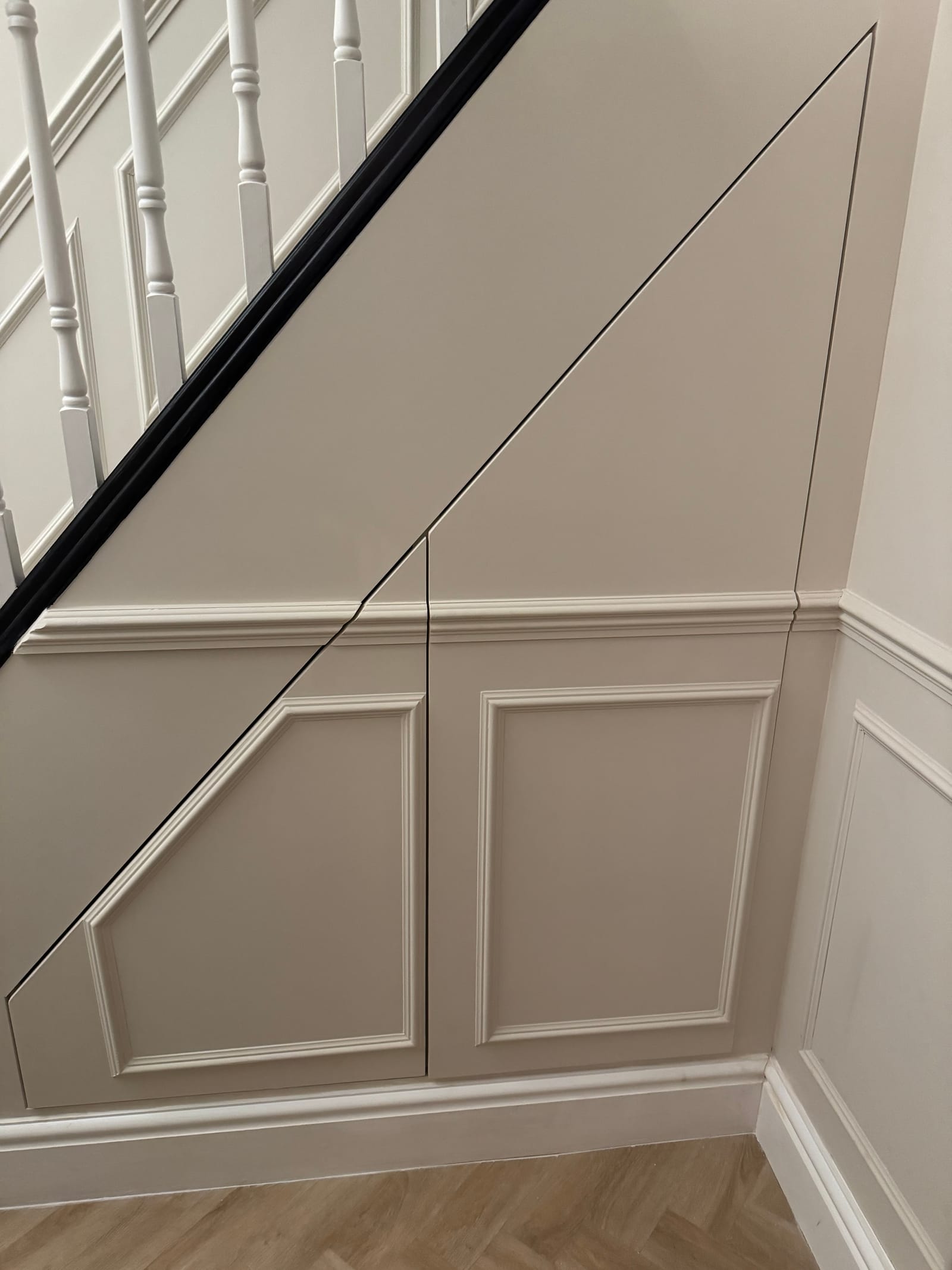 Period under-stair cabinetry detail with cream raised panel doors and parquet flooring