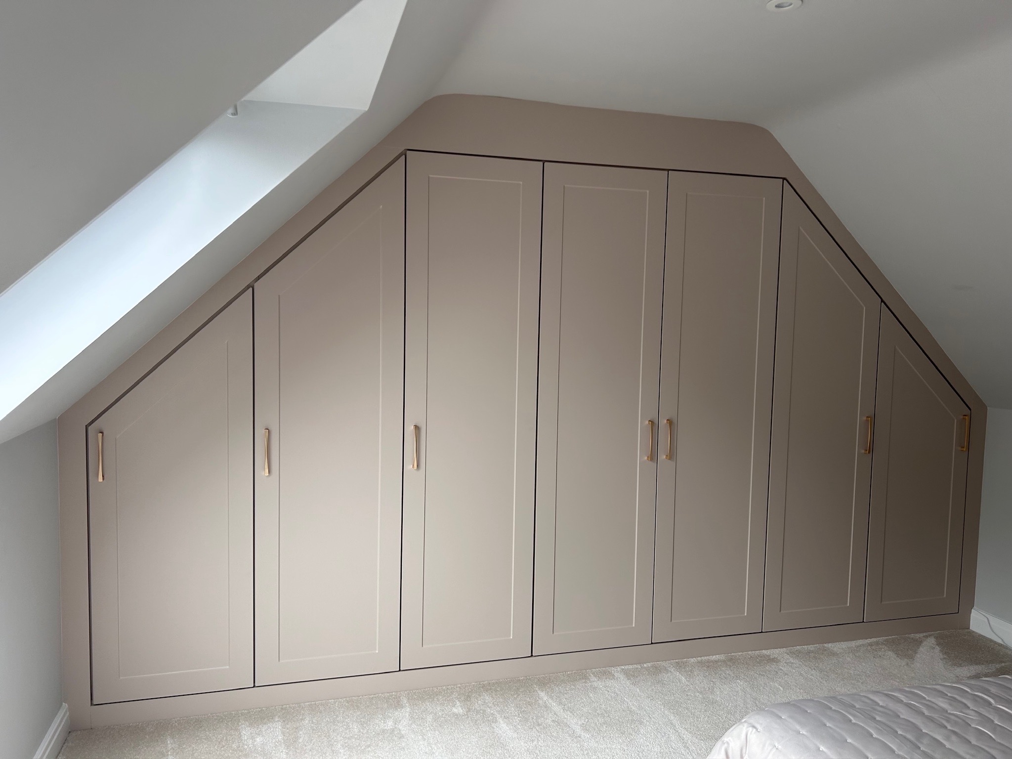 Bespoke fitted shaker wardrobes in a Birmingham loft conversion with angled ceiling and brass handles