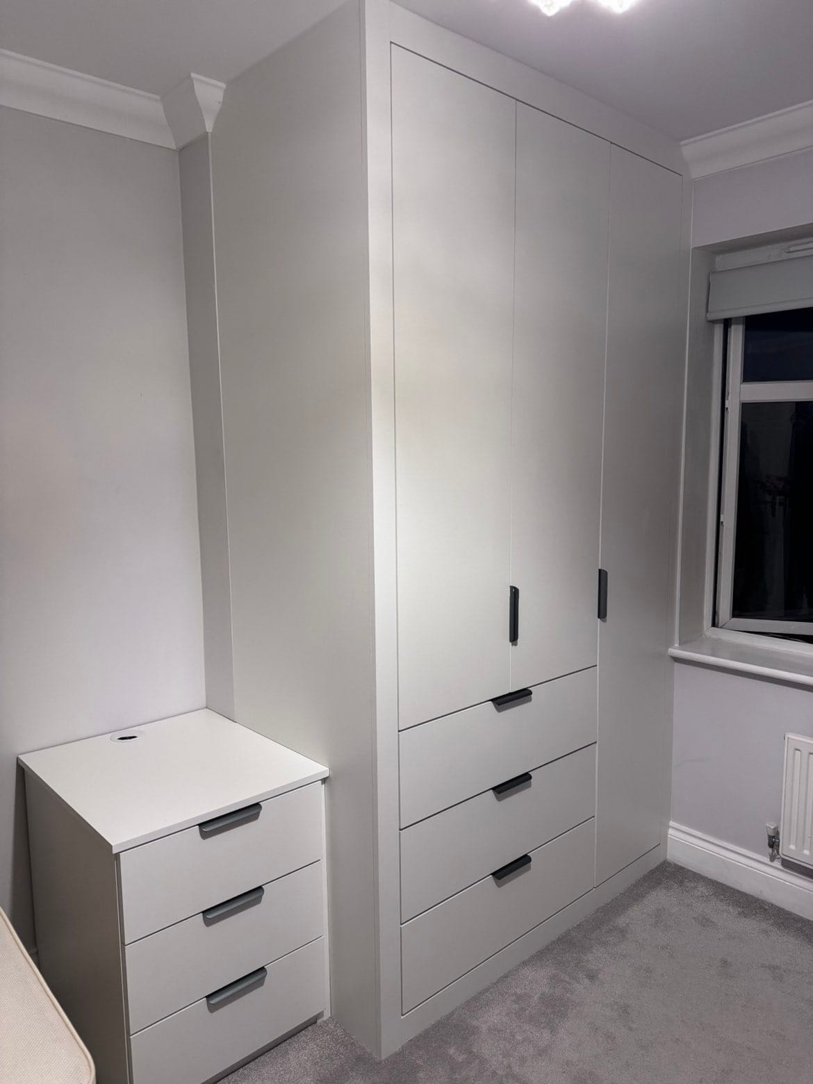 Clean modern white fitted wardrobe with integrated drawers and matching bedside chest