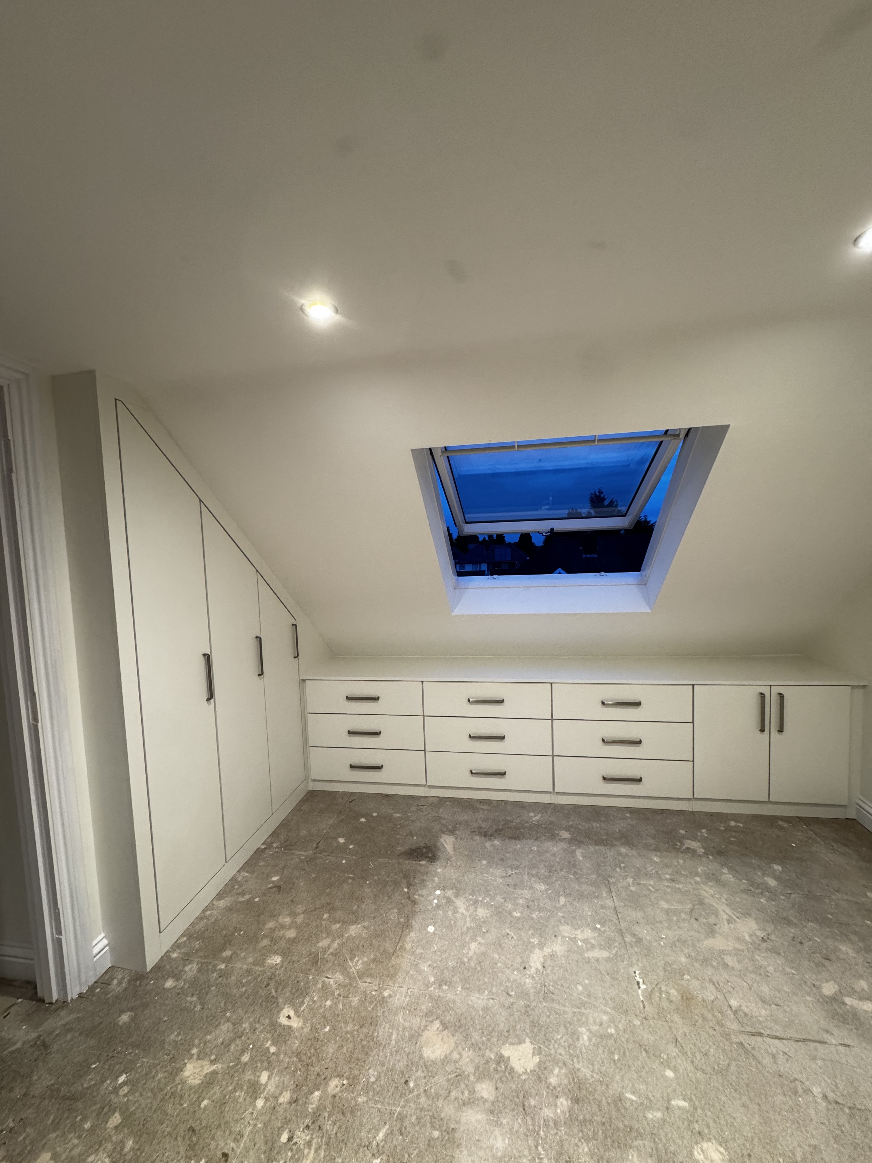 Bespoke loft-eaves fitted wardrobe with a full run of drawers and tall cupboards under a skylight, by SM Bespoke Interiors, Birmingham