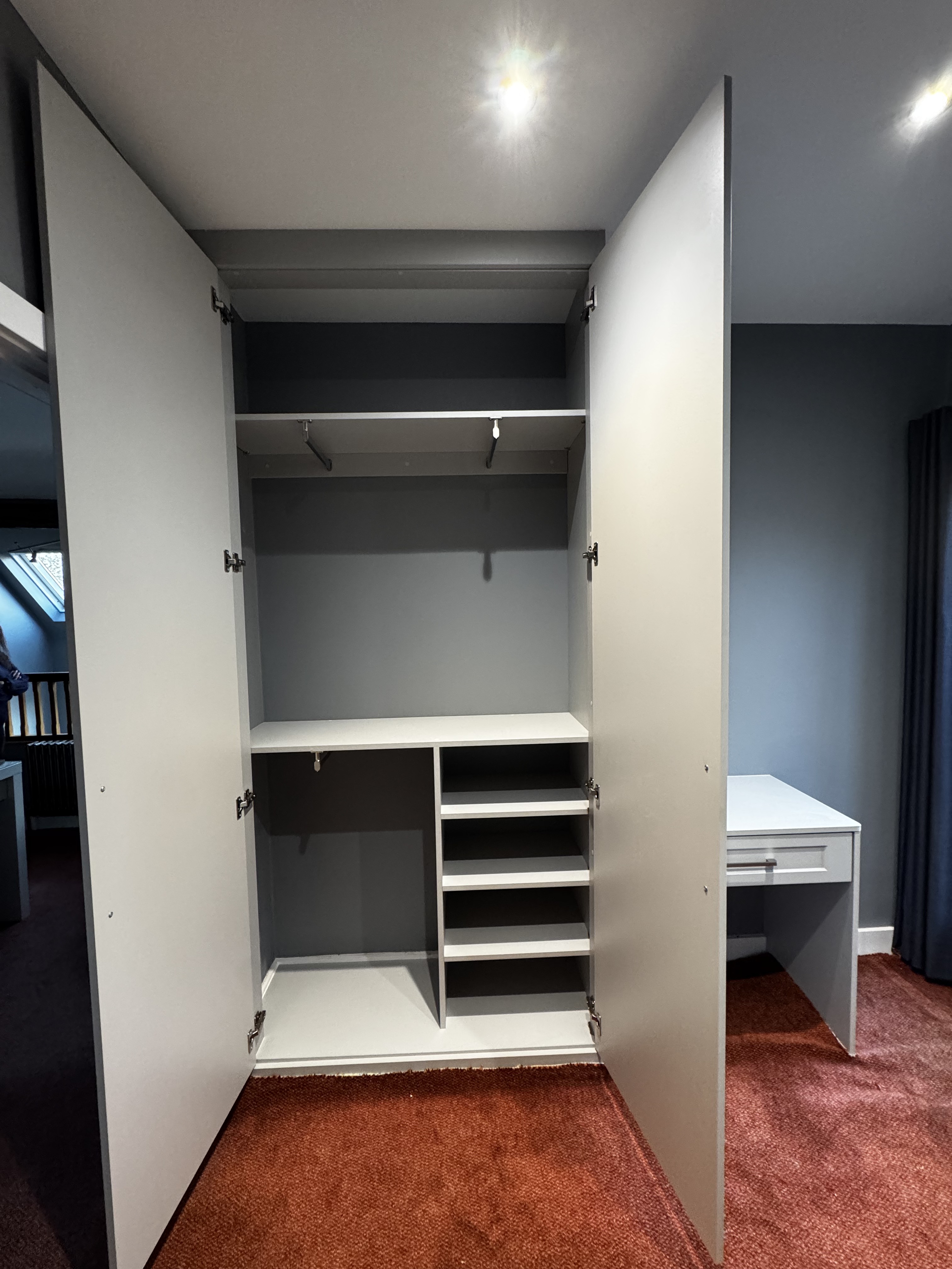 Interior of grey shaker fitted wardrobe with hanging rail, drawers and shoe shelving