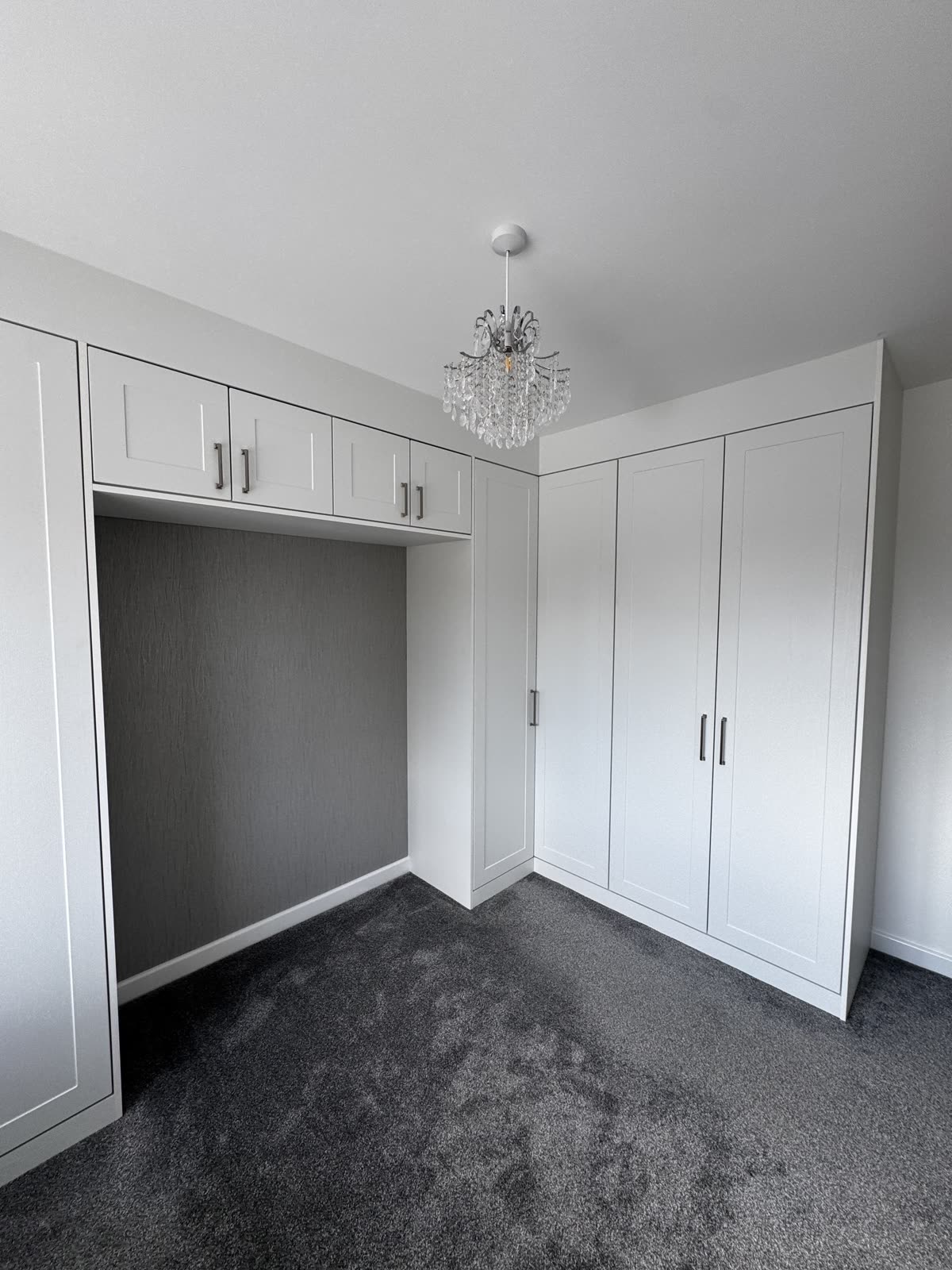 White shaker fitted wardrobes wrapping a bedroom corner, with bridging cupboards over a recess